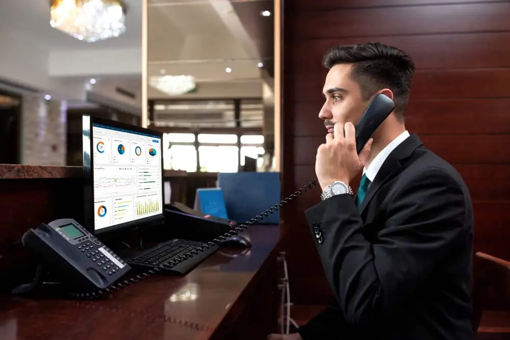 A woman holding a laptop while booking a hotel room, with a phone held to her ear in her other hand